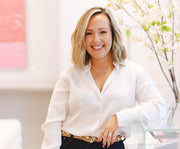 Lindsey Alves standing in a bright, modern room with a glass table and flowering branches in the background.