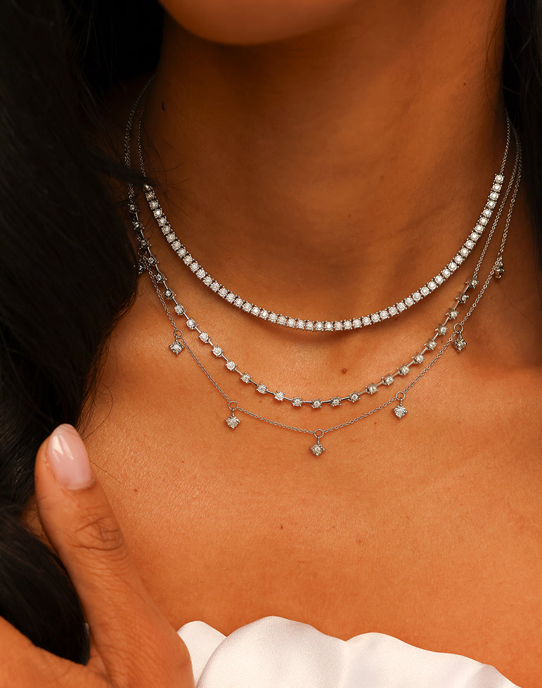 Close-up of a person wearing multiple silver necklaces with small pendants.