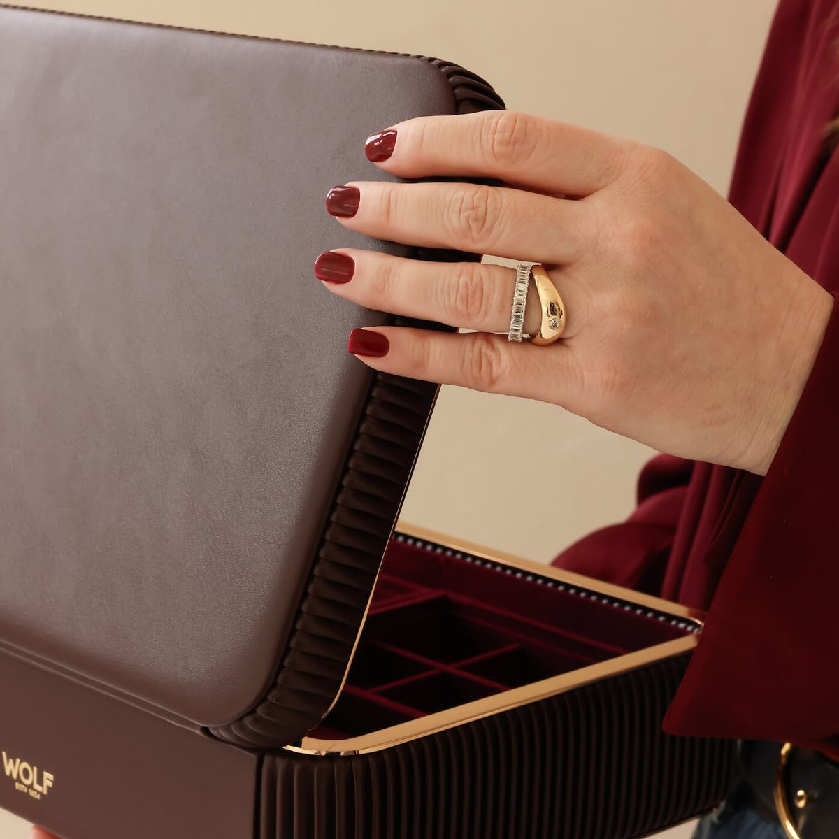 Hand holding a jewelry box with a gold ring, against a neutral background