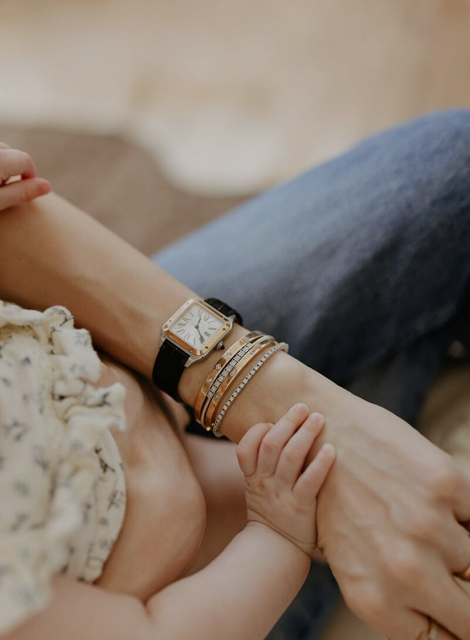 Close-up of a person's wrist with a watch and bracelets, holding a baby's hand.