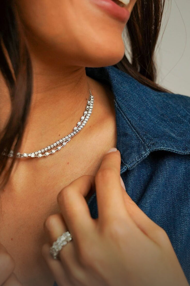 Close-up of a person wearing a white gold and diamond necklace and ring, with a blurred background.