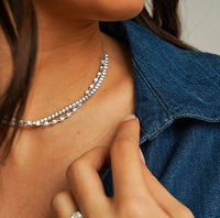Close-up of a person wearing a white gold tennis necklace with a blurred background