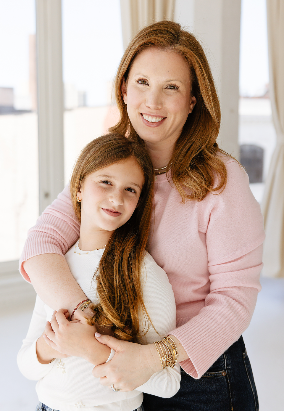 Woman and young girl hugging indoors with a bright background