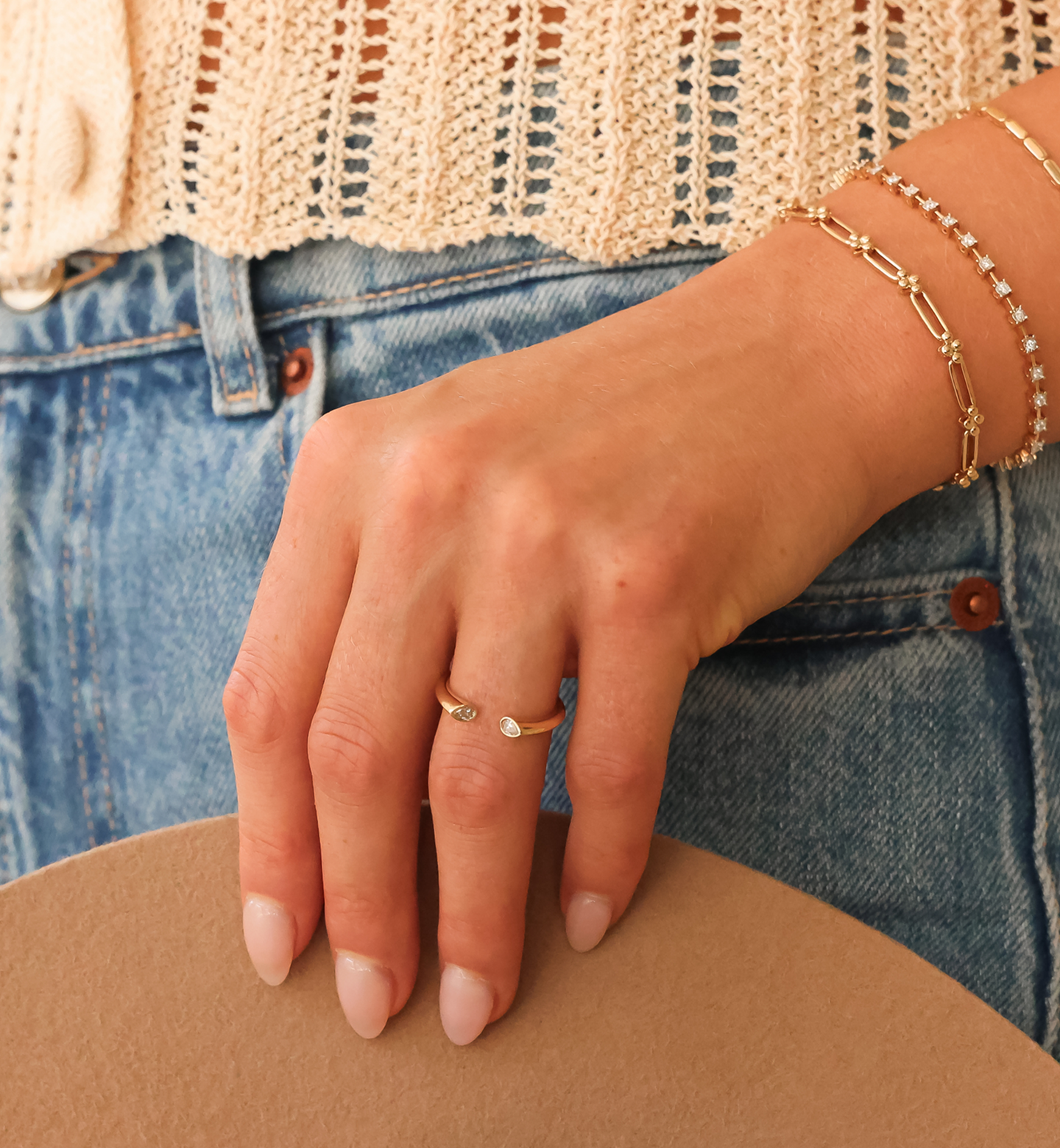 Hand wearing a gold ring and bracelet with denim jeans in the background