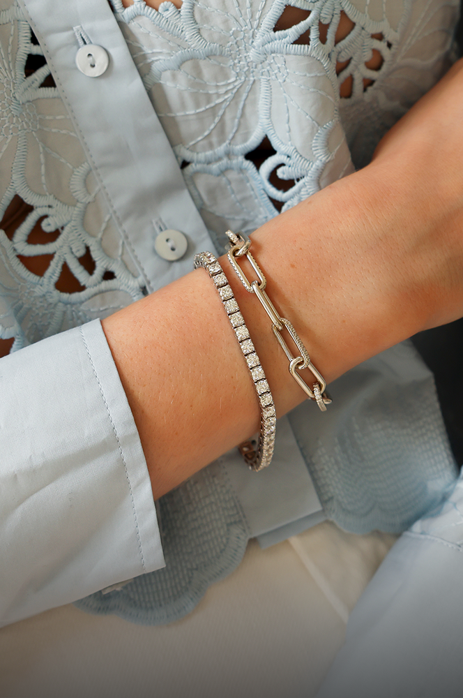 Close-up of a person's wrist wearing a white gold bracelet on a light blue lace shirt background