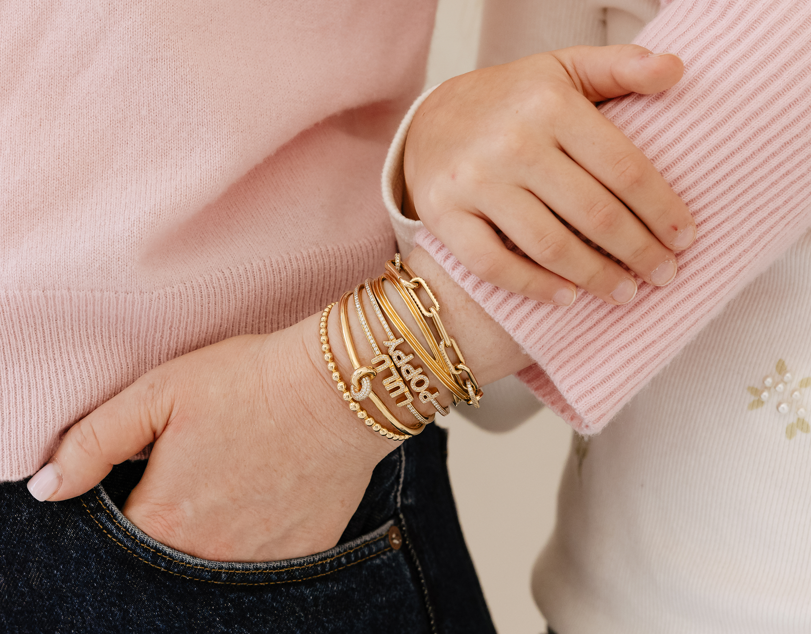 Close-up of a person wearing gold bracelets on a pink sweater background