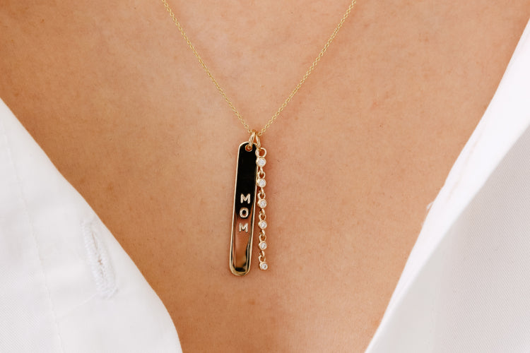 Gold necklace with 'MOM' pendant on a person wearing a white top