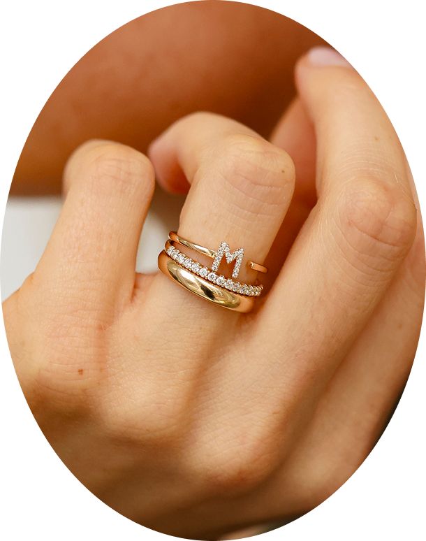 Gold ring with a diamond band on a person's finger, and a diamond initial ring.