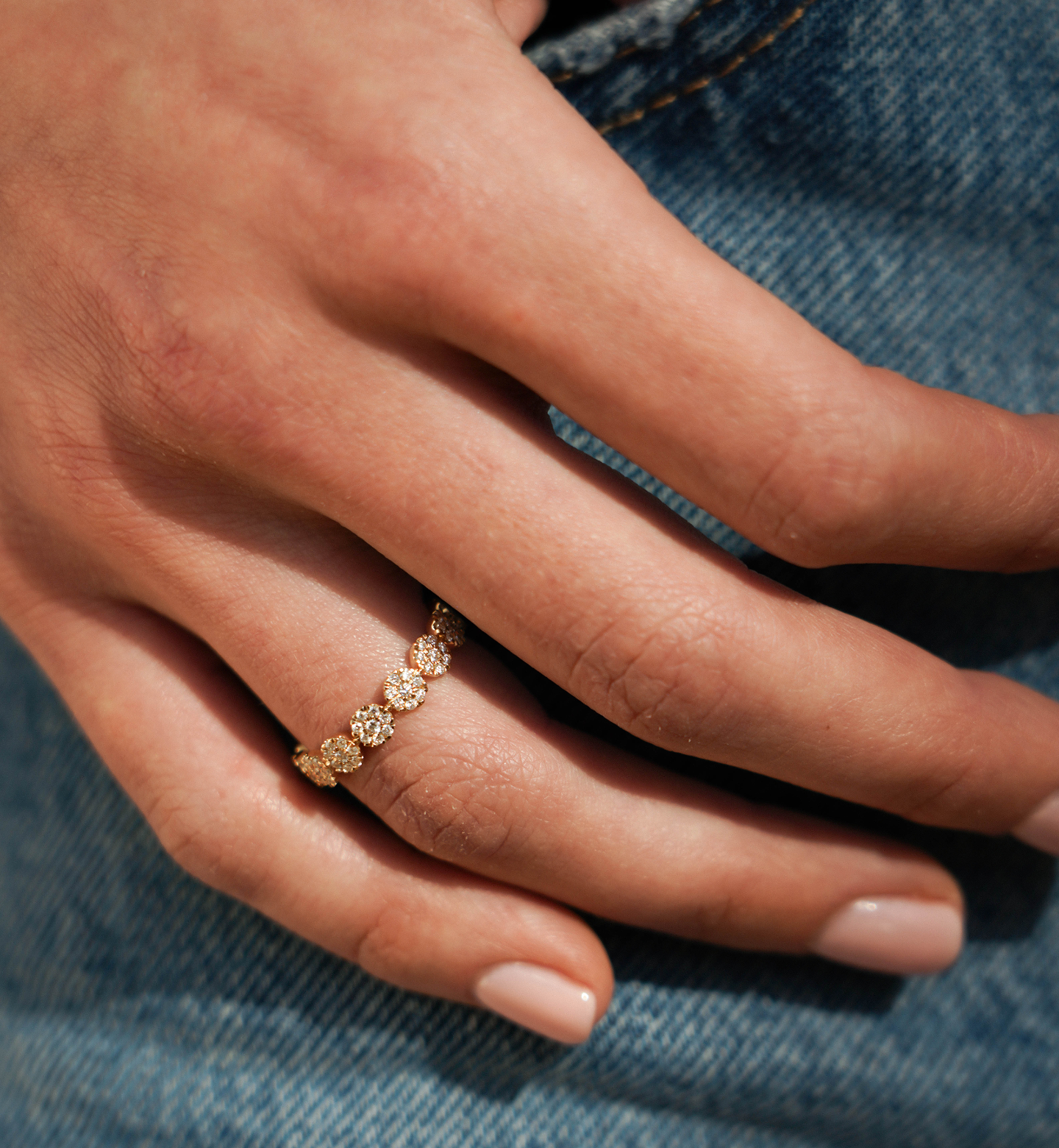 Close-up of a hand wearing a gold ring with floral design on denim fabric