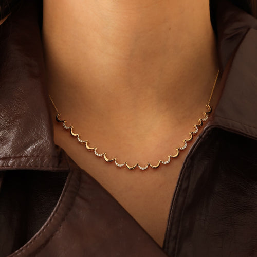 Gold necklace with small stones on a person wearing a brown leather jacket.